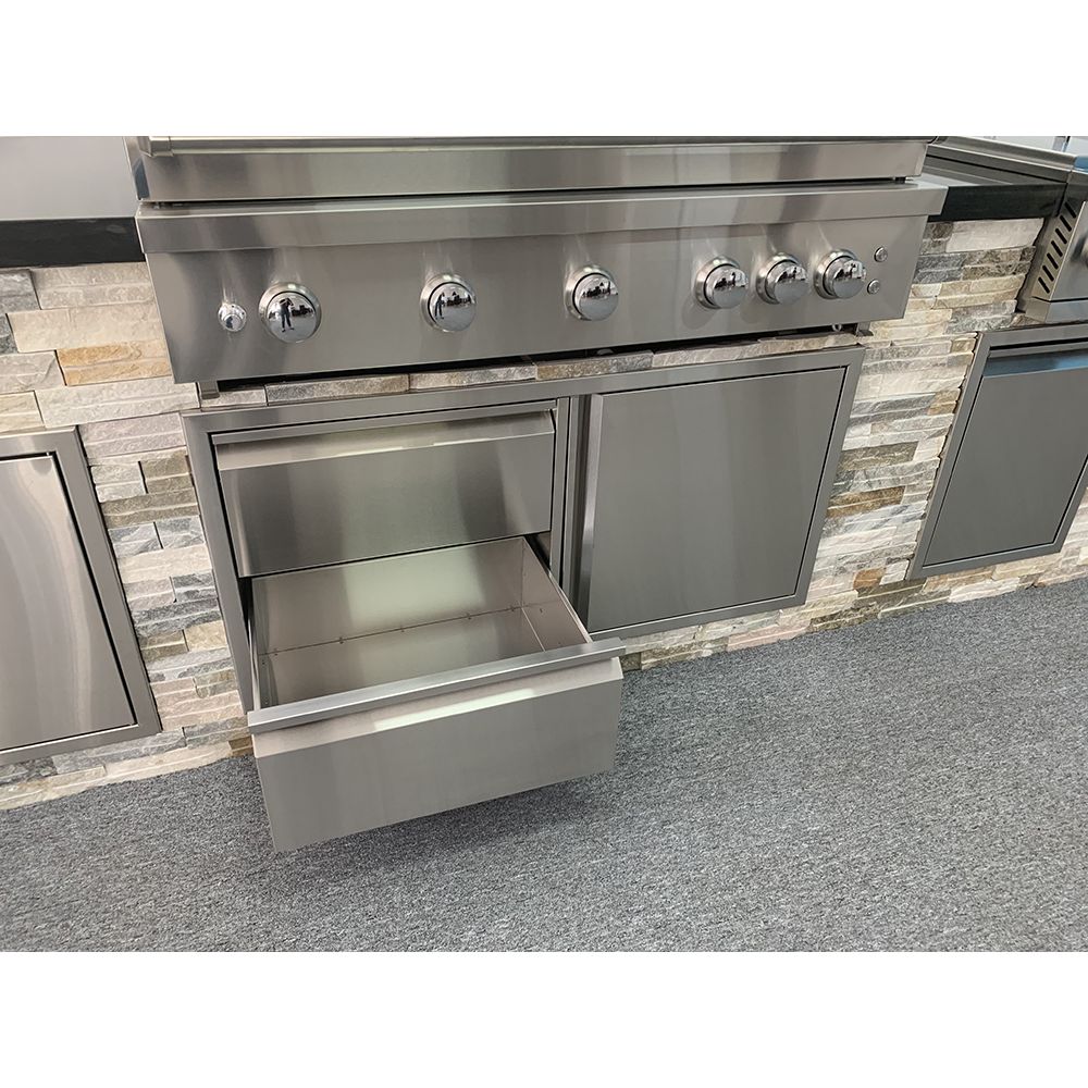 Stainless steel outdoor kitchen grill with open drawer against a stone wall.